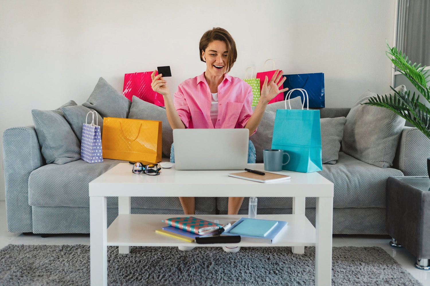 Woman joyfully shopping for electronics shopping online with a laptop and shopping bags around her.